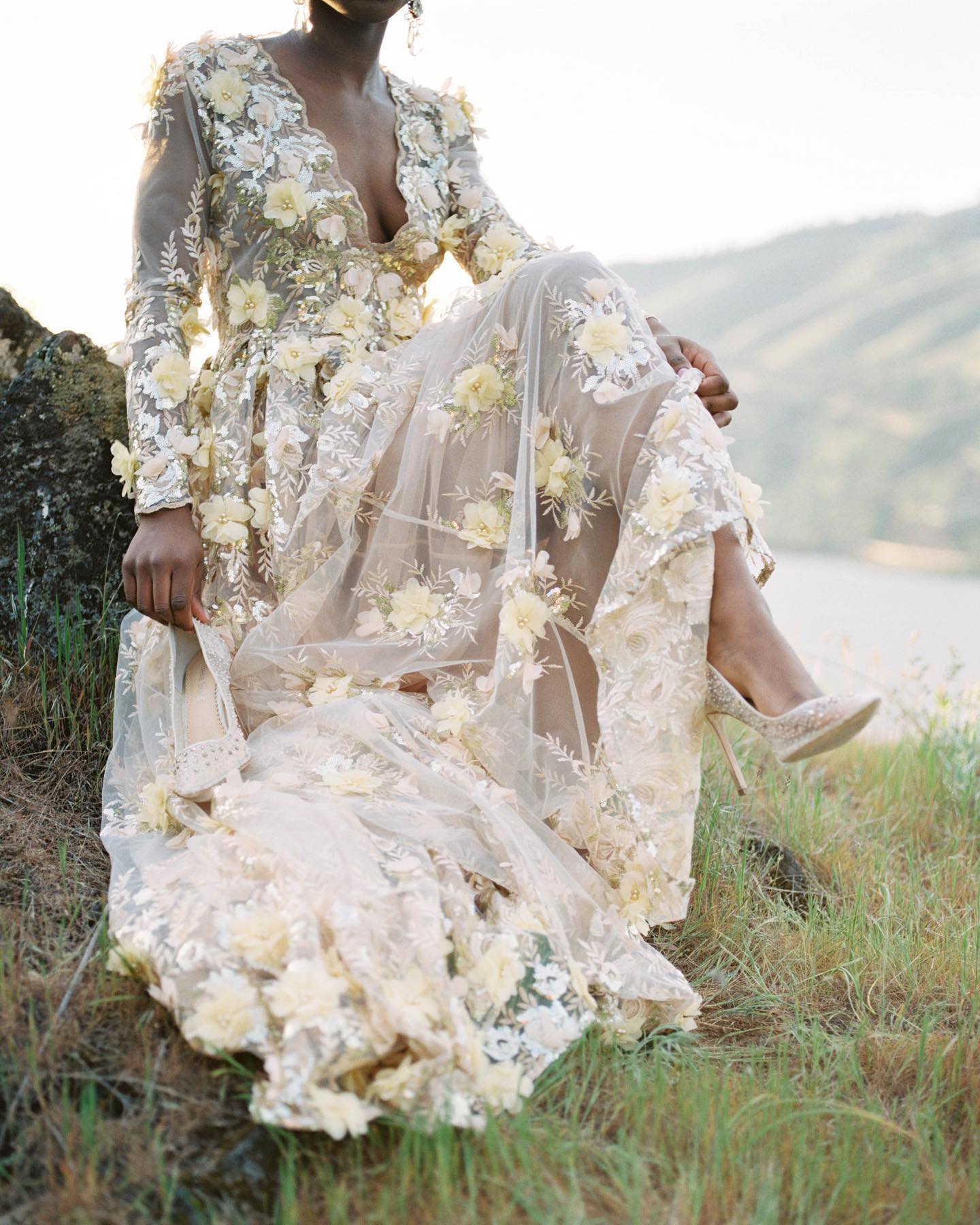 Bride sitting on a large rock in a floral wedding dress holding her shoes near the Columbia Gorge in Hood River OR. Captured by Portland Wedding Photographer Carlos Hernandez